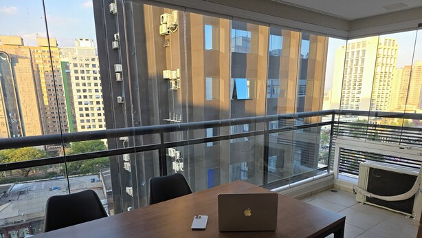 Un espace de bureau moderne doté d’une grande fenêtre, d’une table en bois sur laquelle se trouve un ordinateur portable, et d’une chaise.