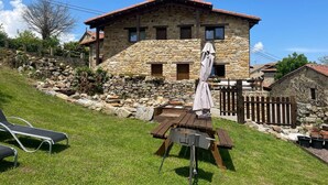 Una casa de piedra con techo inclinado, una terraza de madera y una mesa de picnic.