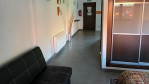 Un pasillo de hotel con un banco de cuero negro, un radiador, un extintor y una puerta con la leyenda 'SALIDA'.