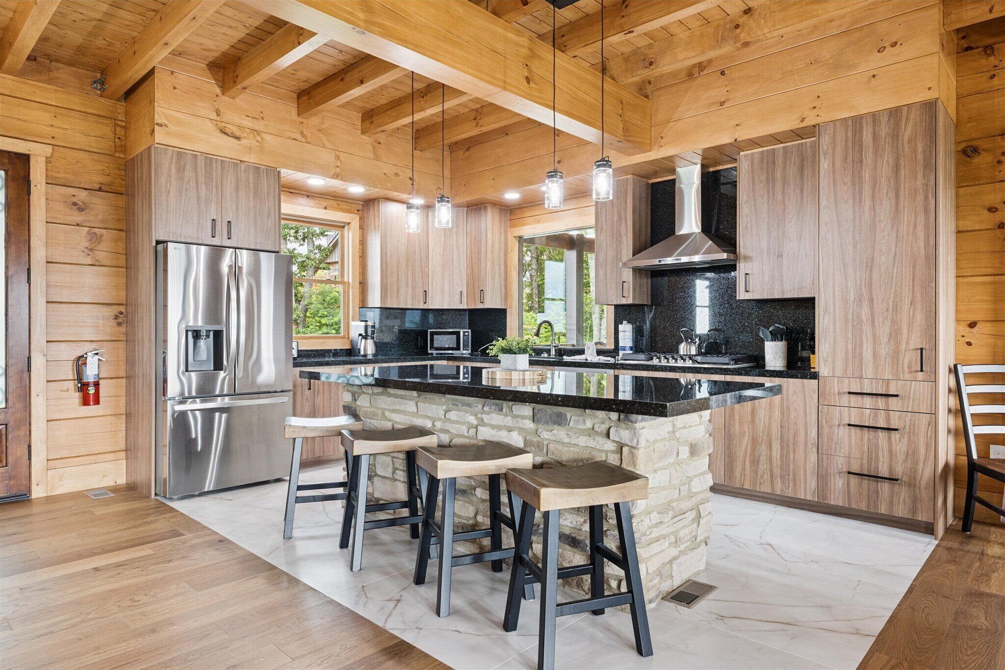 A modern kitchen with wooden walls, a central island with stools, stainless steel appliances, and a stone accent wall.