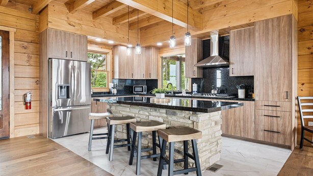 A modern kitchen with wooden walls, a central island with stools, stainless steel appliances, and a stone accent wall.