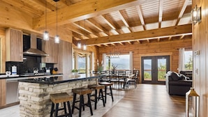 A spacious kitchen with a stone island, wooden bar stools, and a large dining area with a view.