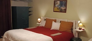 A neatly made bed with a red bedspread and white pillows, flanked by two bedside tables with lamps, a large blue wardrobe, and a painting on the wall. - Aux 10 Ponts - Gîte aux abords du fleuve- Mer à 30min-La nuitée pour 6 voyageurs (Pont-Remy)