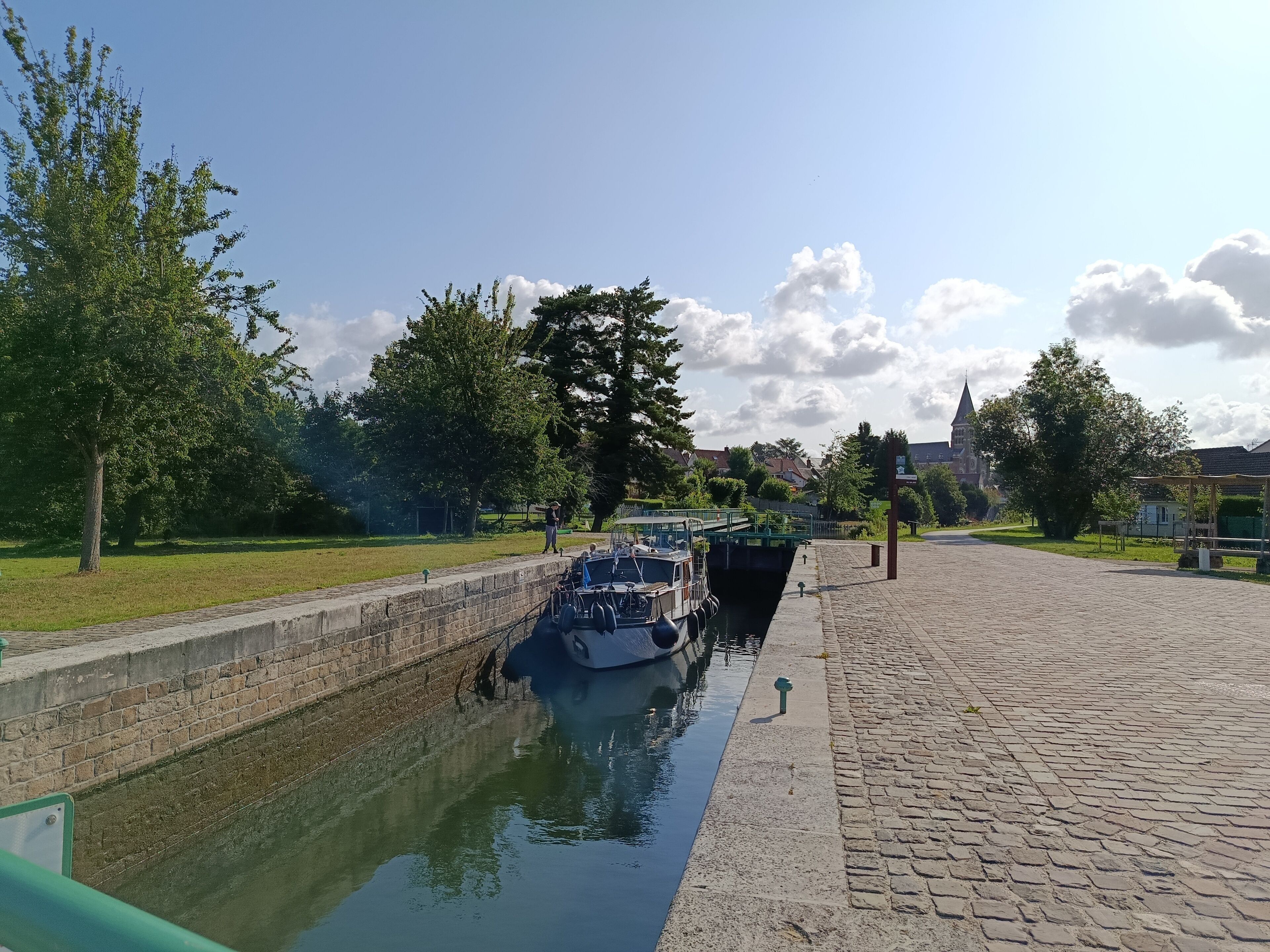 Un canal avec un bateau amarré sur la rive droite, bordé d’arbres et doté d’une promenade pavée.
