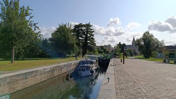 Un canal avec un bateau amarré sur la rive droite, bordé d’arbres et doté d’une promenade pavée.