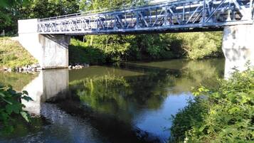 Een metalen brug over een rustige rivier, omzoomd door groen aan weerszijden.