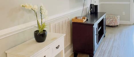 A room with a white console table, a dark wooden cabinet, a flat-screen TV mounted on the wall, and a small white chair.