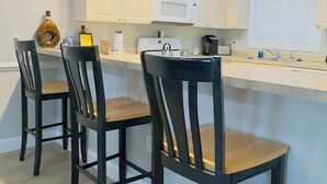 A modern kitchen with white cabinets, a central island with bar stools, and a microwave. - Magnificent 2BR condo, ground floor , Pool (Myrtle Beach)