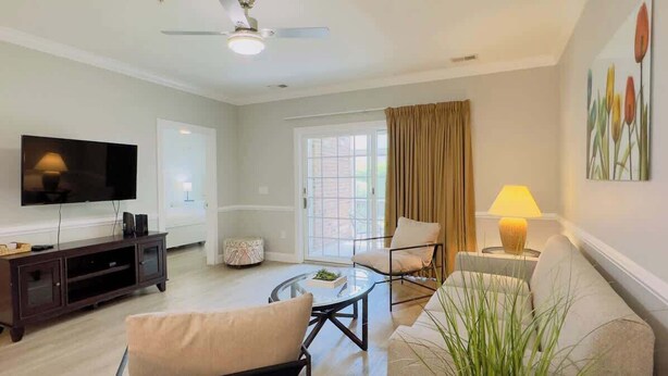A modern living room with a flat-screen TV, a glass coffee table, and a sofa. - Magnificent 2BR condo, ground floor , Pool (Myrtle Beach)