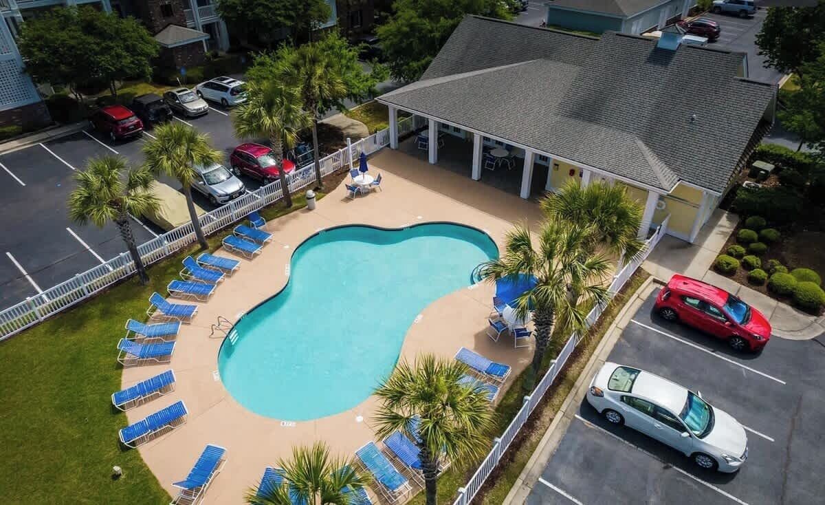 Eine Vogelperspektive zeigt ein Hotel mit Swimmingpool, umgeben von Liegestühlen und Palmen.