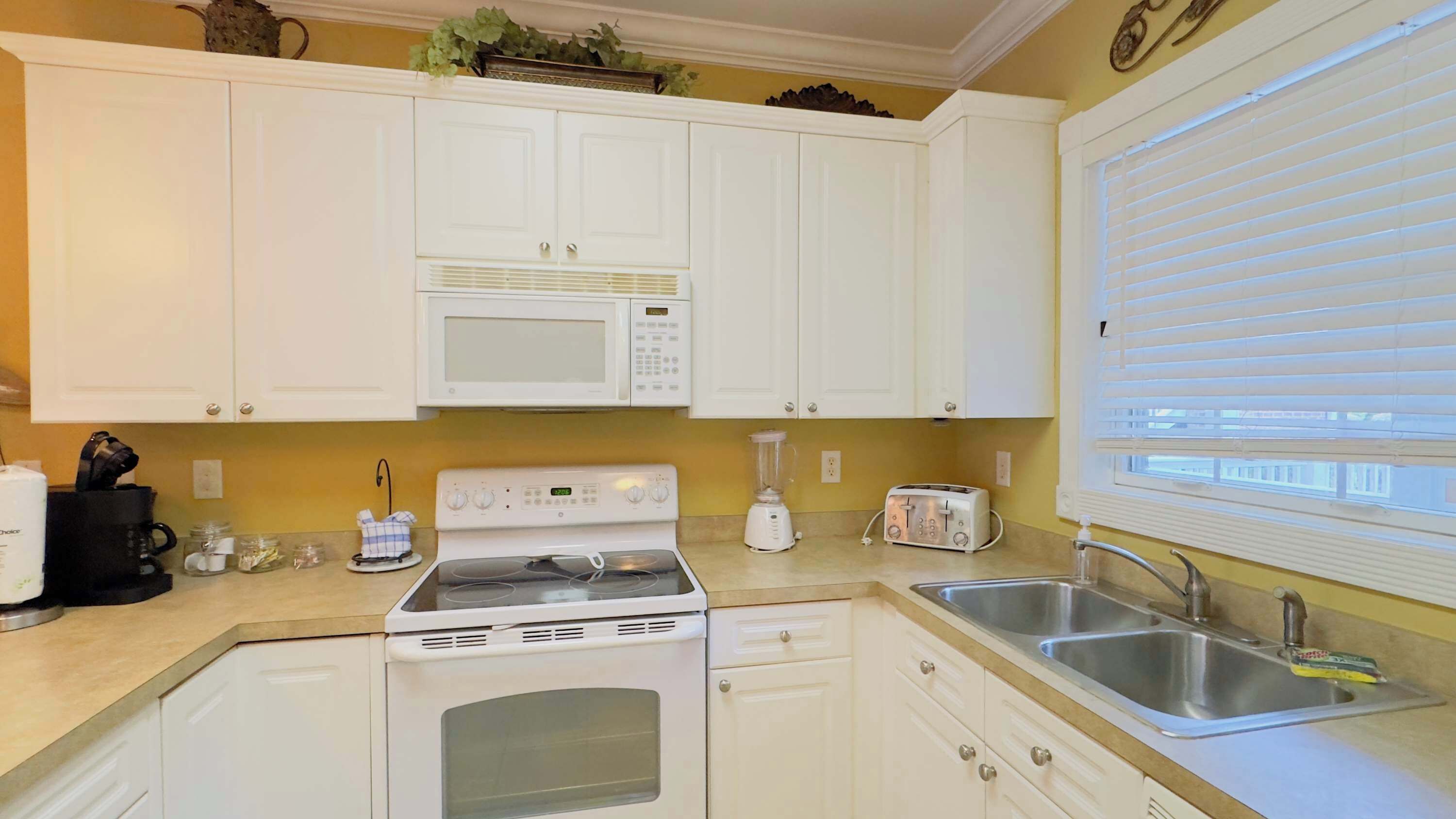 A kitchen with white cabinets, a microwave, a stove, a toaster, and a sink.