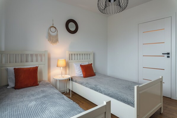A bedroom with two single beds, a bedside table with a lamp, a wall-mounted mirror, and a door with horizontal lines. - Pure Home Premium Apartments (Wroclaw)