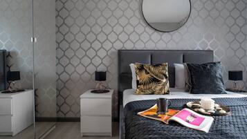 A modern bedroom with a dark quilted bedspread, a bedside table with a lamp, and a nightstand with a lamp.