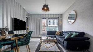 Ett modernt vardagsrum med en svart soffa, gröna fåtöljer, ett soffbord i glas och en platt-TV som är monterad på väggen.