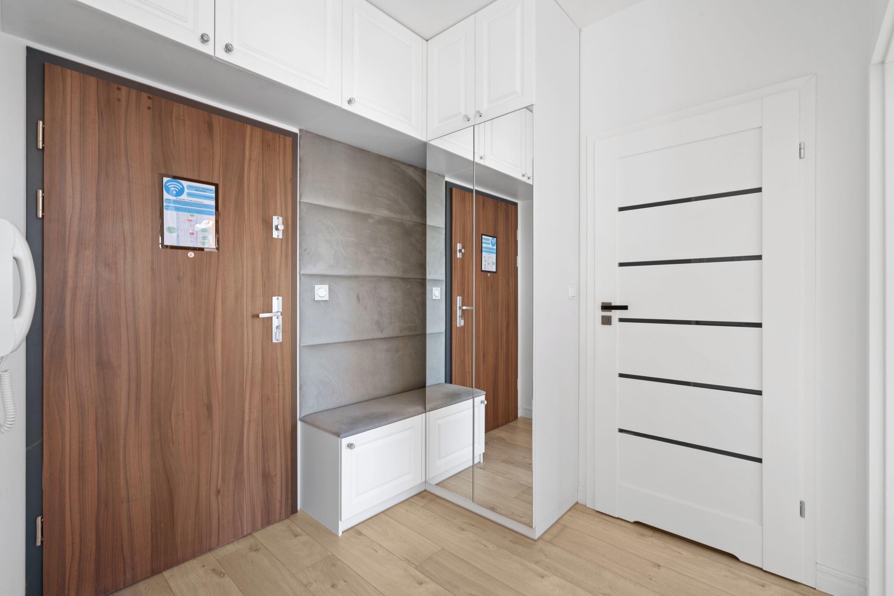 A modern hotel room with a wooden wardrobe, a built-in bench, and a mirrored wardrobe door.