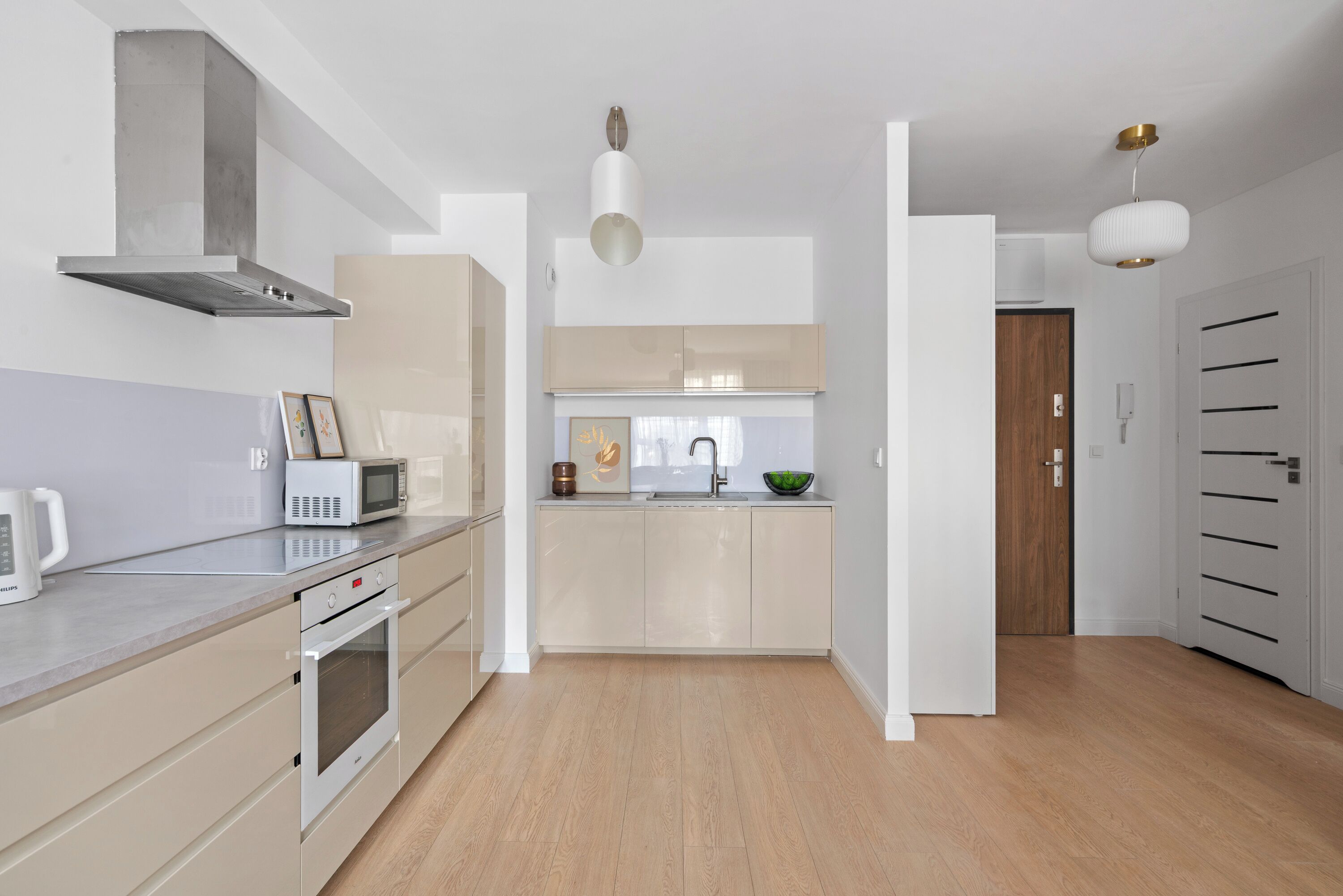 A modern kitchen with a microwave, toaster, and oven. There is a sink with a bowl and a vase on the counter. The kitchen has wooden flooring and white cabinets.