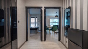 En modern inredning med en hall som leder till en matplats med gröna stolar och ett bord, en soffa och en stor spegel.
