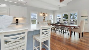 A spacious kitchen with white cabinetry, a marble island, and a dining area with wooden chairs and a large table. - Home Away From Home (Port St. Joe)
