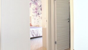 A hallway with a closed door, a bed with a floral-patterned headboard, and a plant in the corner. - Sweet Emily, Panoramic comfort just a stone's throw from Sorrento! (Sant'Agnello)