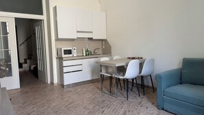 A compact kitchen with white cabinets, a microwave, and a sink. There is a dining table with two chairs and a teal sofa in the living area.