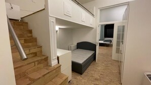 A compact bedroom with a bed, a desk, and a chair. There is a staircase leading to another level.