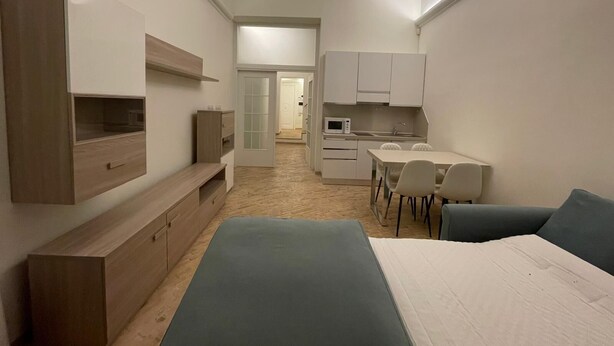 A compact room with a bed, a TV, a kitchenette, and a dining area.