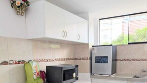 Una cocina con armarios blancos, un microondas, un refrigerador y una mesa con mantel floreado.