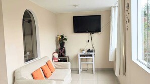 Una sala de estar moderna con un sofá, un televisor de pantalla plana, una mesita y una ventana con cortinas.