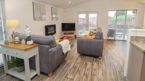 A spacious living area with two grey sofas, a wooden coffee table, a TV, and a sliding glass door leading to a balcony. - Dovedale Lodge (Windermere)