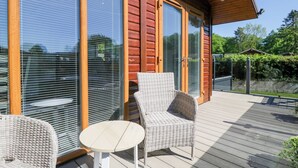 A wooden deck with wicker furniture and a glass door leading to a covered area. - Dovedale Lodge (Windermere)