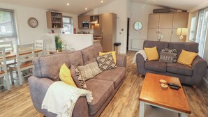 A modern living room with two sofas, a coffee table, and a dining area with a table and chairs. - Dovedale Lodge (Windermere)