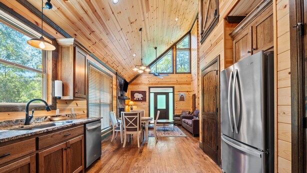 A spacious kitchen with wooden cabinets, a stainless steel refrigerator, and a large window providing natural light. - Standing Bear | Romantic Forest Escape for Couples (Broken Bow)