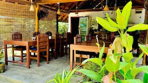 An outdoor dining area with wooden tables and chairs, surrounded by potted plants and a brick wall.