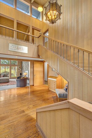 A spacious interior with a wooden staircase, a chandelier, and a view of the outdoors.