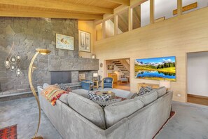 A spacious living area with a stone fireplace, a sofa, a coffee table, and a painting of a mountain landscape.