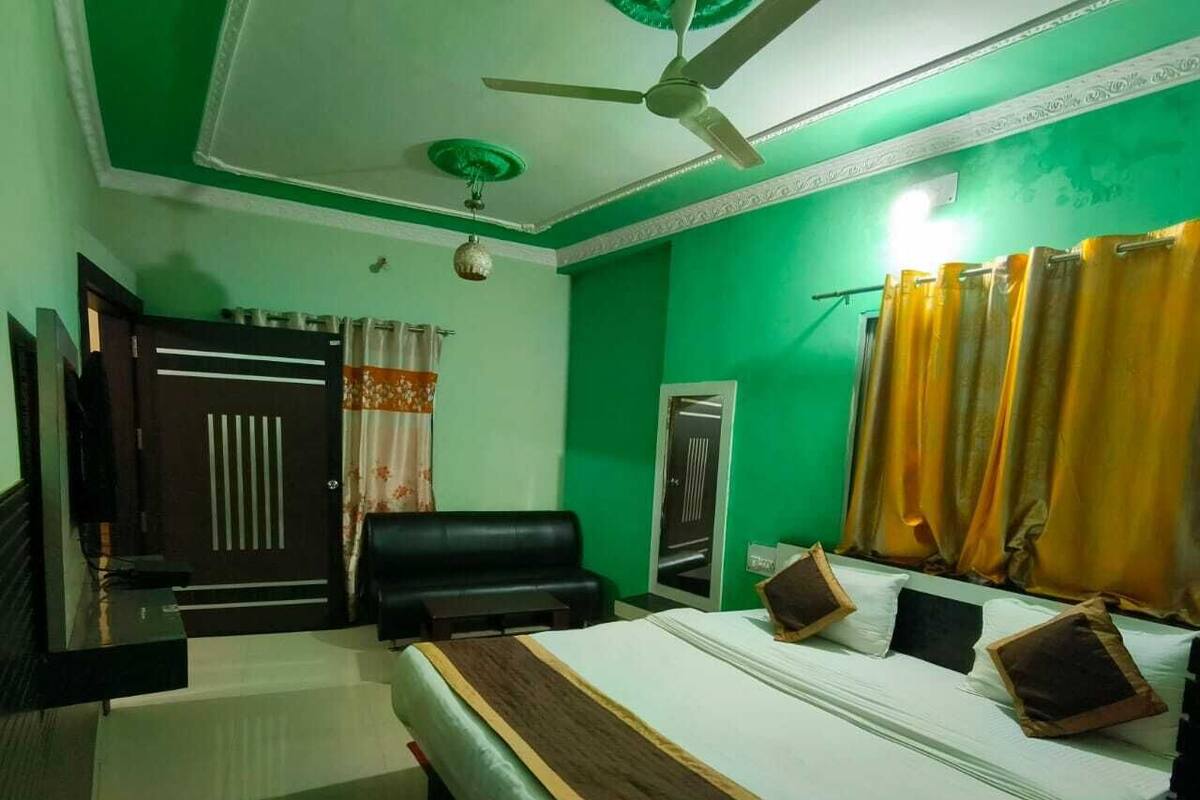 A hotel room with a bed, a black leather sofa, a ceiling fan, and green walls.