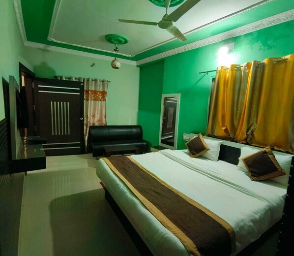 A hotel room with a bed, a black leather sofa, a ceiling fan, and green walls.