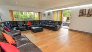 Un salon spacieux avec un grand canapé d’angle en cuir noir, un plancher en bois et de grandes fenêtres dotées de rideaux.