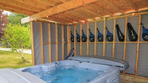 Un bain à remous sous une pergola en bois, avec un mur en bois et une rangée de bouteilles d’eau noires portant l’étiquette « Vermont ».