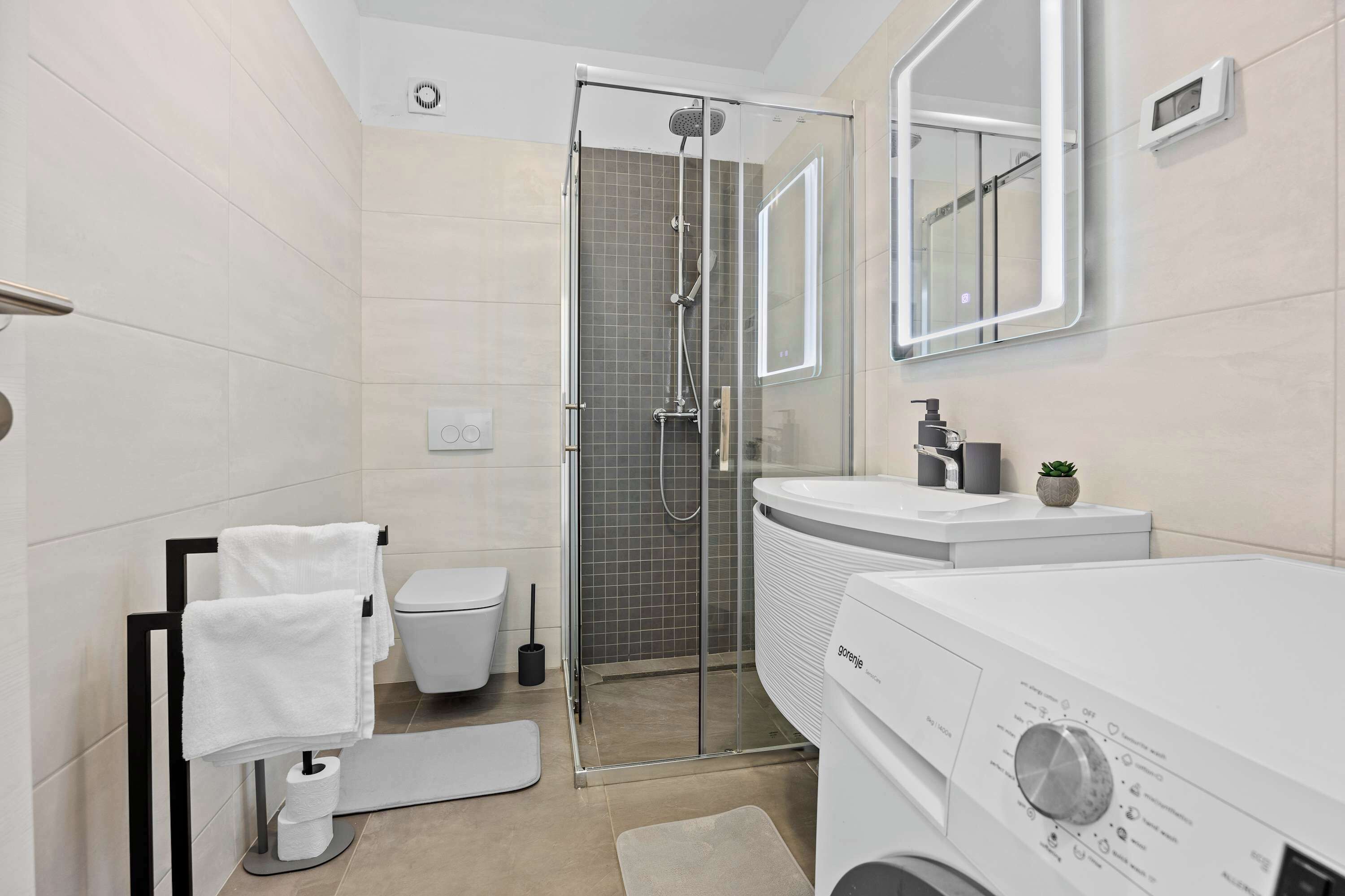 Une salle de bain moderne avec une douche à parois de verre, des toilettes, un lavabo et un lave-linge.