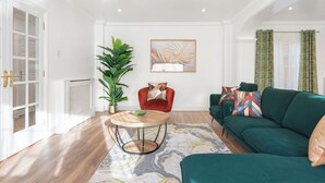 Een woonkamer met een groene bank, een rode fauteuil, een ronde salontafel en een grote groene plant.