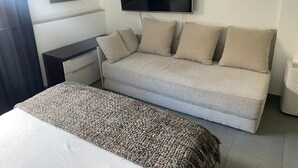 A bedroom with a bed, a sofa, a TV mounted on the wall, and a bedside table.