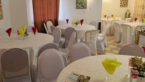 A hotel dining area with round tables covered in white tablecloths, white chairs, and table centerpieces.