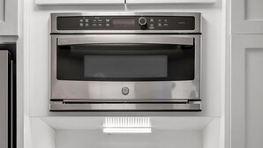 Una cocina moderna con horno empotrado, lavavajillas de acero inoxidable y un armario blanco con picaporte negro.