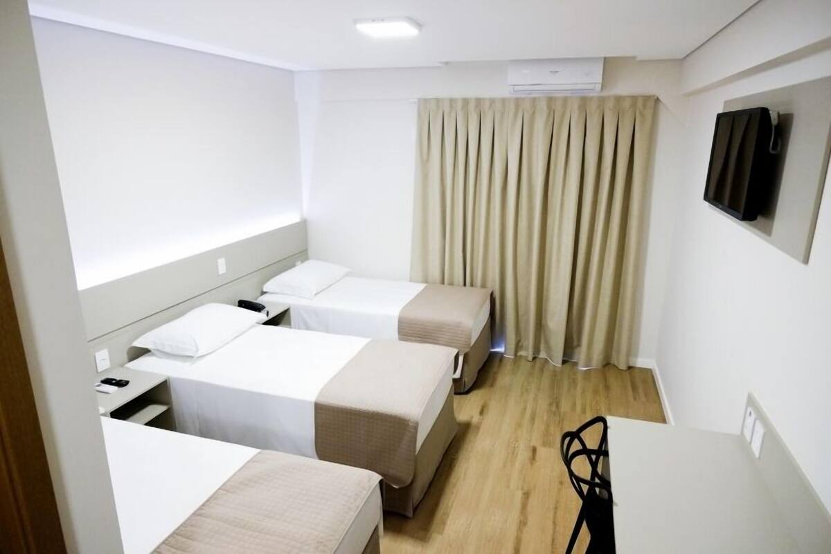 A hotel room with three beds, a desk, a chair, and a television on the wall.