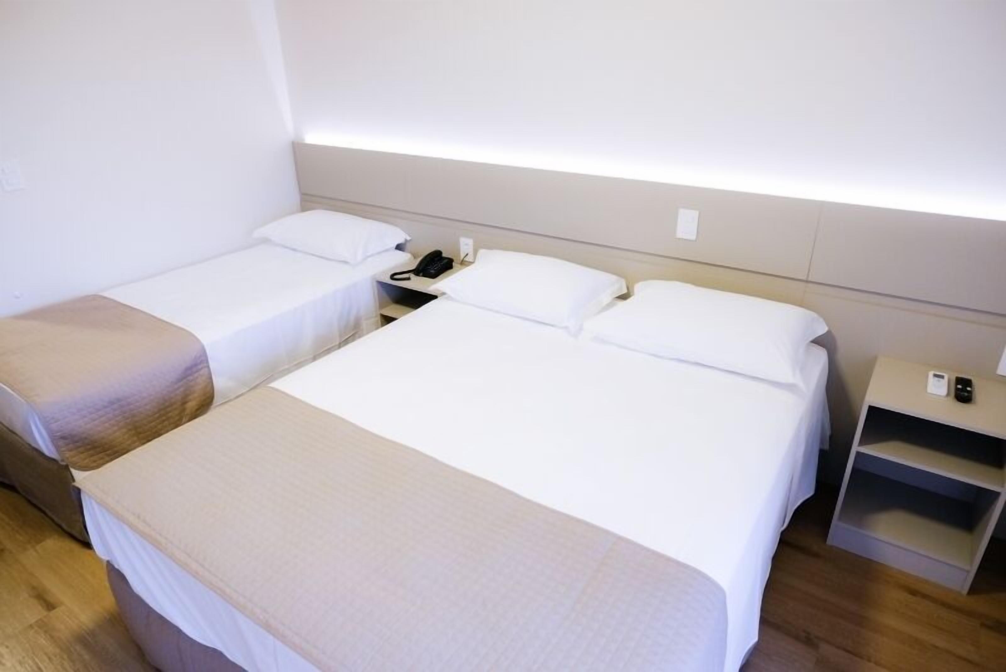 A hotel room with two single beds, a bedside table with a phone, and a small shelf unit.