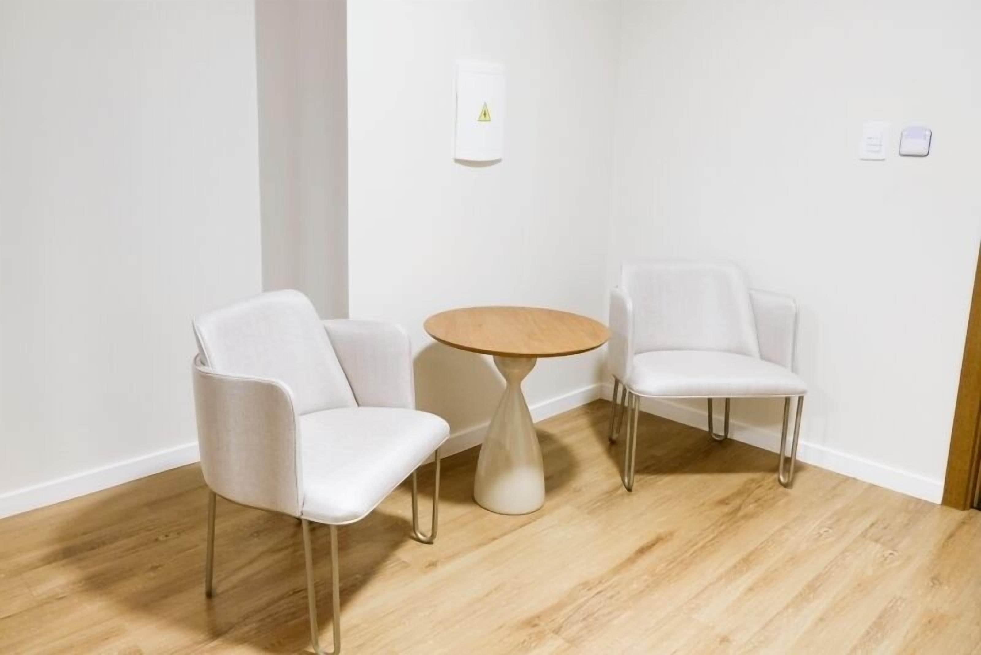 Habitación de esquina con dos sillas blancas y una pequeña mesa de madera.