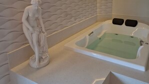 A modern bathroom with a marble wall, a freestanding bathtub, and a marble statue. - Gringo Hotel (Erval Velho)