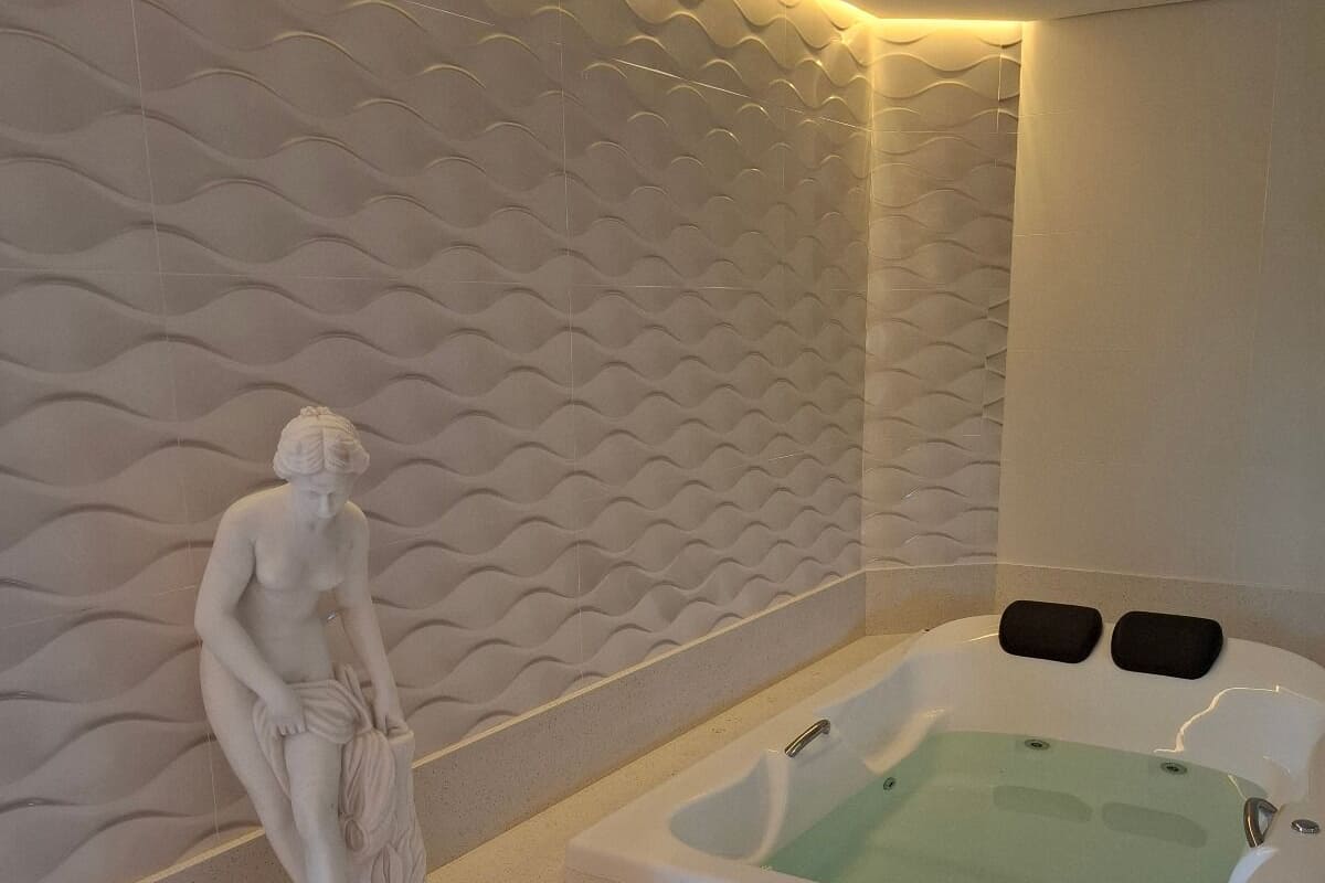 A modern bathroom with a marble wall, a freestanding bathtub, and a marble statue.