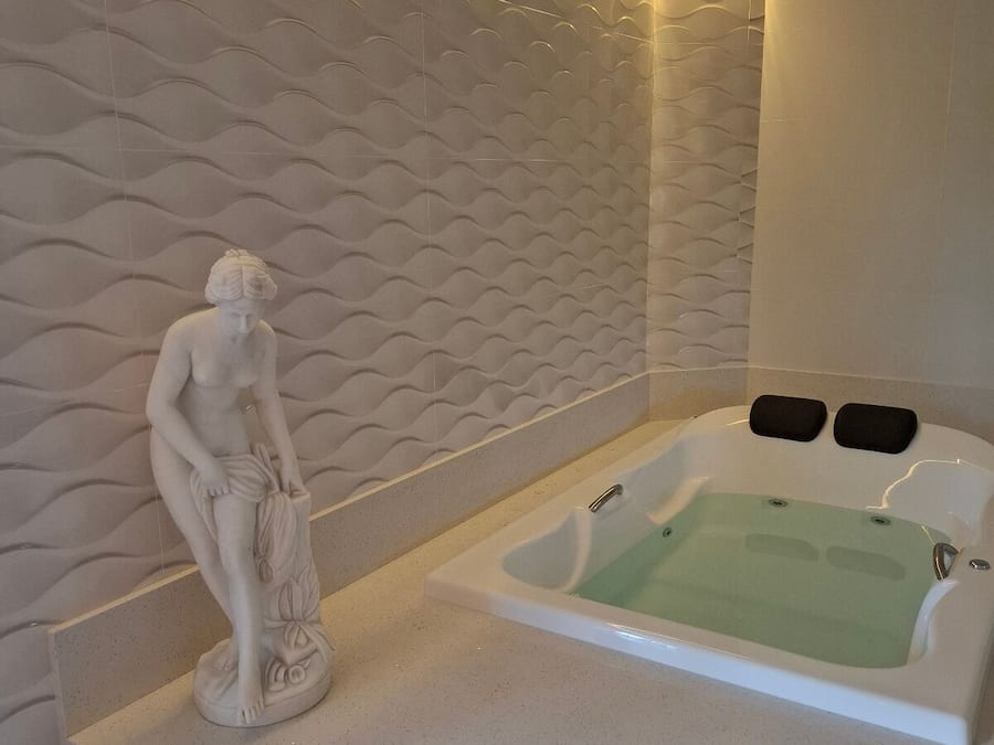 Un baño moderno con pared de mármol, una bañera independiente y una estatua de mármol.